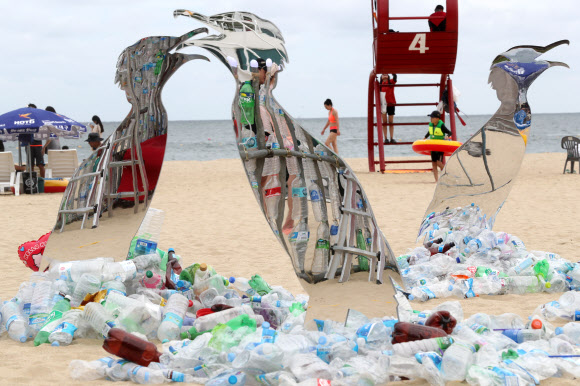 13일 부산 해운대구 해운대해수욕장에 일회용 플라스틱을 이용해 만든 미술작품 뒤로 피서객이 지나가고 있다. 그린피스는 이날부터 사흘간 해운대해수욕장에서 일회용 플라스틱으로 만들어진 미술작품을 통해 플라스틱 사용에 대한 경각심을 일깨우고 일회용 플라스틱 소비를 줄이는 방안에 대해 알릴 예정이다.  연합뉴스