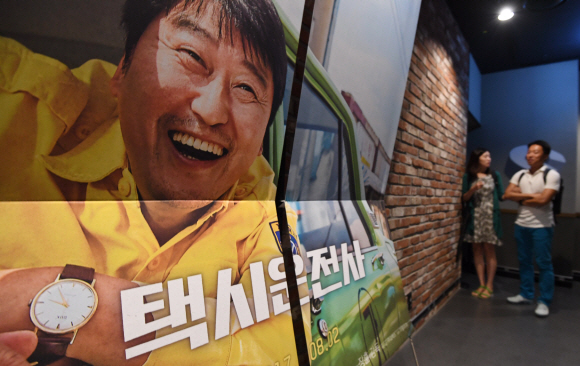 5.18 광주민주화운동을 소재로 한 영화 ’택시운전사’가 누적관객수 천만을 돌파해 올해 첫 ’천만 영화’로 기록된 20일 서울 용산의 한 영화관에서 관람객들이 ’택시운전사’ 포스터 앞을 지나가고 있다. 2017. 8. 20. 박윤슬 기자 seul@seoul.co.kr