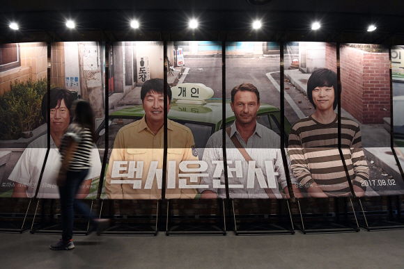 5.18 광주민주화운동을 소재로 한 영화 ’택시운전사’가 누적관객수 천만을 돌파해 올해 첫 ’천만 영화’로 기록된 20일 서울 용산의 한 영화관에서 관람객들이 ’택시운전사’ 포스터 앞을 지나가고 있다. 2017. 8. 20. 박윤슬 기자 seul@seoul.co.kr