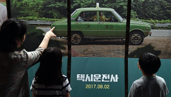 5.18 광주민주화운동을 소재로 한 영화 ’택시운전사’가 누적관객수 천만을 돌파해 올해 첫 ’천만 영화’로 기록된 20일 서울 용산의 한 영화관에서 관람객들이 ’택시운전사’ 포스터를 바라보고 있다. 2017. 8. 20. 박윤슬 기자 seul@seoul.co.kr