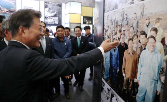 문재인 대통령이 15일 오후 충남 태안군 만리포해수욕장 일원에서 열린 ’함께 살린 바다 희망으로 돌아오다’ 서해안유류피해 극복 10주년 행사에서 참석자들과 함께 유류 피해 극복 기념관을 둘러보던 중 고 노무현 대통령과 함께 촬영한 사진을 가리키고 있다. 연합뉴스.