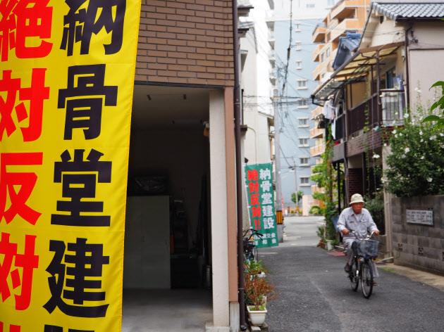 일본 오사카의 한 주택가에 납골당 건설 절대 반대 문구가 적힌 플래카드 옆을 한 주민이 자전거를 타고 지나가고 있다.