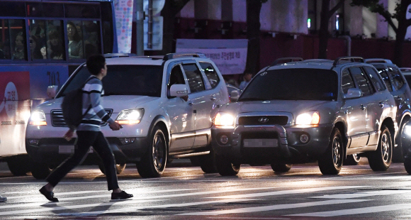교통신호를 준수하는 운전 습관이 교통사고를 줄일 수 있는 가장 기본적인 자세다. 지난 20일 밤 서울 중구 횡단보도를 건너는 시민 너머로 승용차와 버스가 나란히 서 있다. 손형준 기자 boltagoo@seoul.co.kr