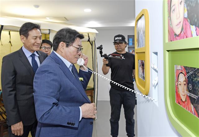 김기동 광진구청장이 지난달 27일 서울 마포구 유니세프 한국위원회 어린이지구촌 체험관을 찾아 수화기로 어려움에 처한 지구촌 어린이의 육성 녹음을 듣고 응원의 메시지를 보내고 있다. 유니세프 한국위원회 친선대사인 배우 안성기씨가 뒤에서 웃음을 짓고 있다. <br>광진구 제공