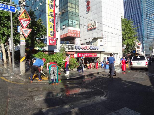 우시장 상인들이 올해 9월 시장 진입로이자 공동 주차장 바닥에 묻어 있는 기름때를 제거하고 있다.<br>금천구 제공