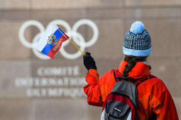  한 여성이 5일(현지시간) 스위스 로잔의 국제올림픽위원회(IOC) 본부 건물 외벽의 오륜 마크 앞을 러시아 국기를 흔들며 지나가고 있다. IOC 집행위원회는 러시아 선수단의 2018 평창동계올림픽 참가를 막기로 결정했다. 로잔 AP 연합뉴스 