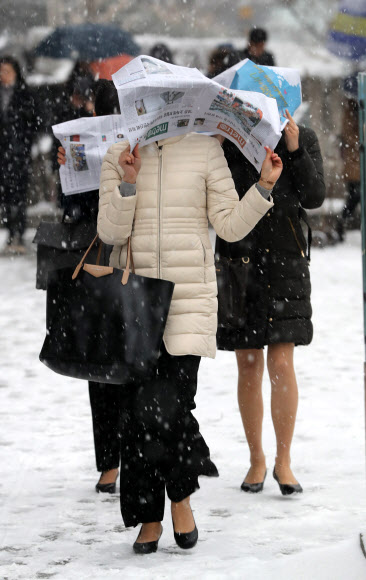 18일 오전 광화문에서 시민들이 신문지로 눈을 피하며 출근하고 있다.  연합뉴스