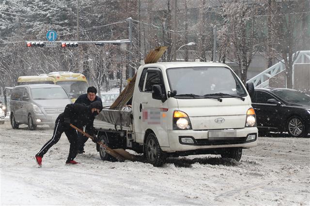수도권 지역에 대설주의보가 내려진 18일 오전 서울 서초구 서울중앙지방법원 앞 도로에서 시민들이 차를 밀며 언덕길을 오르고 있다. 뉴스1