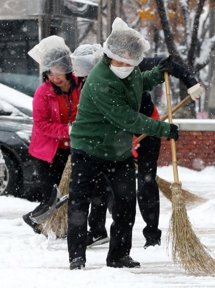 18일 오전 서울 여의도 한 건물에서 관계자들이 비닐봉지를 쓰고 내리는 눈을 치우고 있다.  연합뉴스