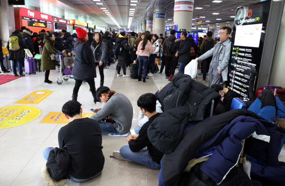 11일 제주공항에 강풍을 동반한 폭설이 내리면서 항공편이 무더기로 결항하자 관광객들이 공항 대합실에 주저앉은 채 항공편이 운항하길 기다리고 있다.  연합뉴스