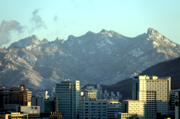 밤사이 한파가 시작된 23일 오전 서울 여의도에서 바라본 북한산에는 하얀 눈이 내려 아침 햇살을 받고 있다. 마포 당인리 발전소 굴뚝에서는 추운 날씨로 수증기가 공기 중으로 솟아오르고 있다.  연합뉴스