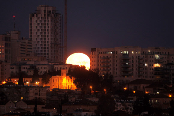 31일(현지시간) 예루살렘 도시 건물 사이로 달이 밝은 빛을 내뿜으며 떠오르고 있다. 개기월식이 일어날 것으로 예견된 이날은 35년 만에 ‘슈퍼문’, ‘블루문’, ‘블러드문’ 총 3가지 천문현상이 관측될 것으로 보인다. AFP 연합뉴스