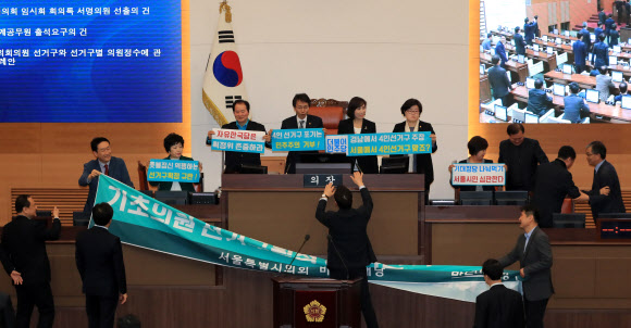 20일 오후 서울시의회 본회의장에서 바른미래당 소속 의원들이 더불어민주당과 자유한국당 소속 의원들 항의 속에 4인 선거구 확대를 요구하며 의장석을 점거한 채 농성을 벌이고 있다.  연합뉴스