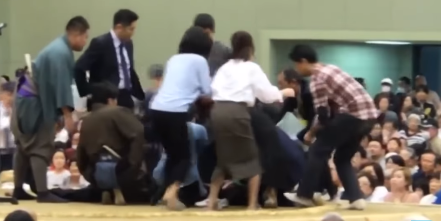 지난 4일, 일본 스모협회는 교토부 마이즈루시에서 열린 대회 도중 졸도한 사람을 응급처치하려고 씨름판으로 올라간 여성에게 “내려가라”는 방송을 하고 소금을 뿌려 거센 비판에 휩싸였다. = 유투브 영상 캡쳐