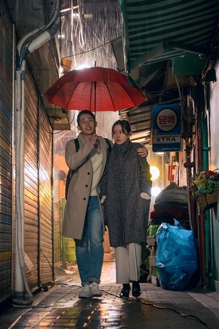 ‘밥 잘 사주는 예쁜 누나’에서 정해인(왼쪽)과 손예진이 빨간 우산을 함께 쓰고 가로등 불빛 아래 빗길을 걸어가는 장면. <br>JTBC 제공
