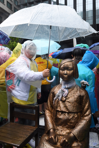 16일 오전 서울 종로구 중학동 일본대사관 앞에서 열린 제1335차 일본군성노예제 문제 해결을 위한 정기 수요시위에 참가한 학생이 우산으로 소녀상을 씌워주고 있다. 도준석 기자 pado@seoul.co.kr