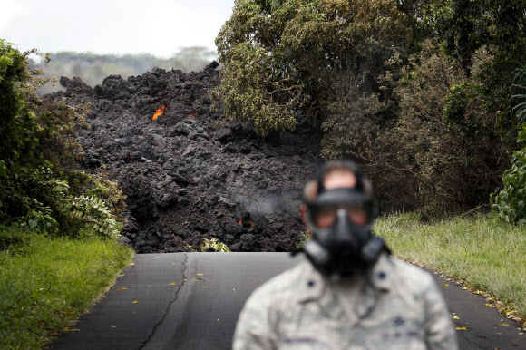 하와이 빅아일랜드 킬라우에아 화산 폭발로 파호아 지역에 용암이 흘러내리고 있는 사진을 19일(현지시간) 미국 지질조사국이 공개했다. 방독면을 쓴 사람 뒤로 흘러내린 용암이 도로를 덮치고 있다. AP 연합뉴스