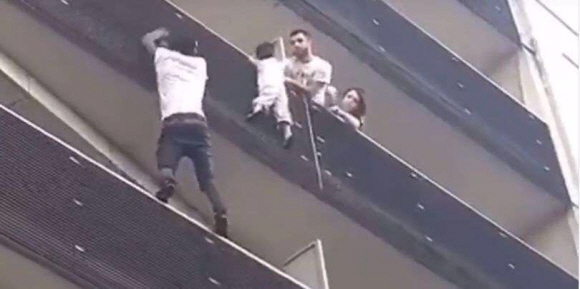 아프리카 말리 출신 청년 마무두 가사마(왼쪽 아래)가 지난 26일(현지시간) 프랑스 파리 18구의 한 아파트 5층 발코니 손잡이에 매달린 4살짜리 아이를 구출하기 위해 이웃집 주민들(오른쪽)이 지켜보는 가운데 맨몸으로 아파트 발코니를 기어올라가고 있다. 트위터 캡처