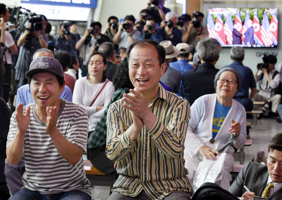 역사적 북·미 정상회담이 열린 12일 서울역 로비에 많은 시민이 모여 도널드 트럼프 미국 대통령과 김정은 북한 국무위원장의 첫 만남 생중계 장면을 보며 박수를 치고 있다.  교도 AP
