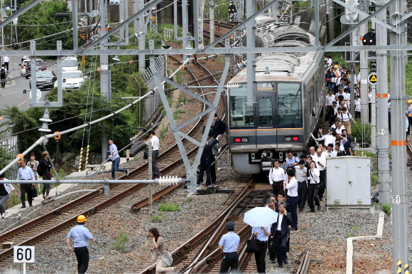 18일 오전 일본 오사카에서 지진이 발생한 가운데 지진으로 멈춰 선 열차에서 승객들이 빠져나와 철길을 걷고 있다. 이번 지진은 규모 5.9로 추정된다고 일본 기상청은 밝혔다.  AFP 연합뉴스