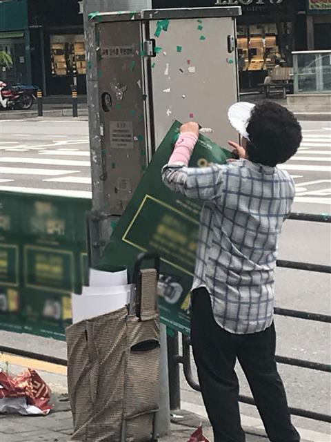 지난달 27일 오후 2시쯤 60대로 보이는 여성이 서울 동작구 노량진 동작경찰서 앞 교통단속용 무인장비에 공무원 입시학원 광고 포스터를 붙이고 있다. 고혜지 기자 hjko@seoul.co.kr