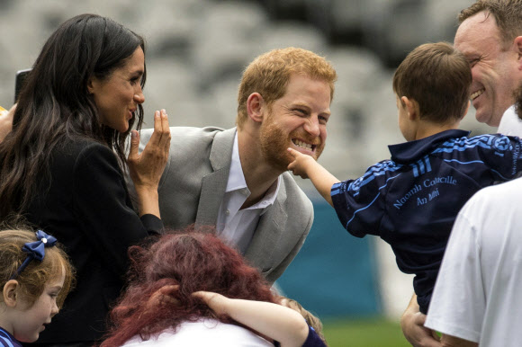 영국 서식스 공작 해리 왕자(가운데)와 서식스 공작부인 메건(왼쪽)이 11일(현지시간) 아일랜드 더블린을 방문한 두 번째 날 크로크 파크 (Croke Park)에서 어린 아이가 해리 왕자의 수염을 만져 웃으며 아이를 바라보고 있다. AP 연합뉴스