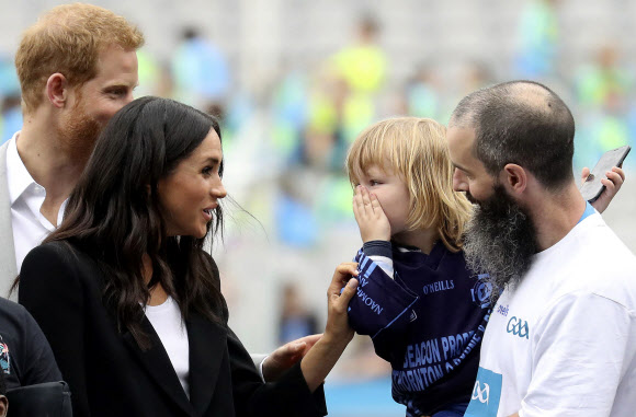 영국 서식스 공작 해리 왕자(왼쪽 뒤)와 서식스 공작부인 메건(왼쪽)이 11일(현지시간) 아일랜드 더블린을 방문한 두 번째 날 크로크 파크 (Croke Park)에서 어린 아이가 서식스 공작부인 메건의 머리카락을 만져 아이를 보고 웃고 있다. AP 연합뉴스