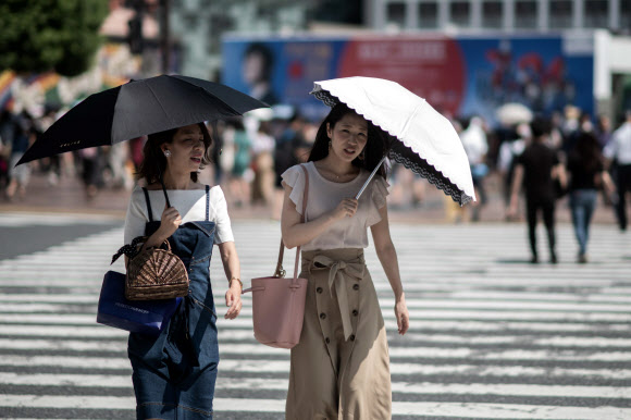 23일 일본 도쿄에서 양산을 쓴 시민들이 횡단보도를 건너고 있다. 이날 NHK를 비롯한 일본 매체는 도쿄도 오우메시의 최고 기온이 40.8℃까지 치솟는 등 무더위가 계속되고 있다고 전했다. AFP 연합뉴스
