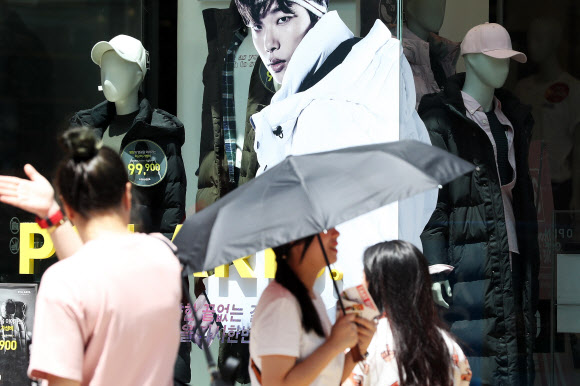 주말 기온이 36도까지 오른 12일 오후 서울 중구 명동 쇼핑가에서 롱패딩을 입은 마네킹이 설치된 쇼윈도 앞으로 양산을 든 시민 등이 걷고 있다. 2018.8.12  연합뉴스