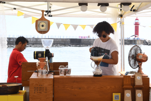 ‘에딧의 커피스토리’로 마켓에 참가 중인 오명자 셀러가 푸른 바다와 등대를 배경으로 주문받은 드립 커피를 내리고 있다.