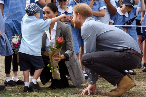 영국의 해리 왕자가 17일(현지시간) 호주 더보 두보지역 공항에 도착해 메건 마클 왕자비가 환영나온 부니용 공립학교의 학생과 포옹를 하고 있는 것을 지켜보고 있다. AFP 연합뉴스