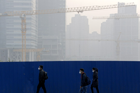 13일(현지시간) 스모그로 뒤덮인 중국 베이징의 센트럴 비즈니스 지역 공사장 옆을 마스크를 쓴 사람들이 지나가고 있다. 2018.11.13 AP 연합뉴스