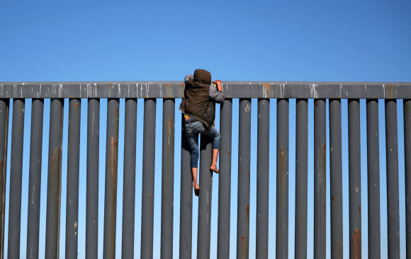 중미 출신 이민자 행렬(캐러밴)중 한 명이 18일(현지시간) 멕시코 티후아나의 미국과 멕시코 국경 펜스에 올라가 있다. 로이터 연합뉴스