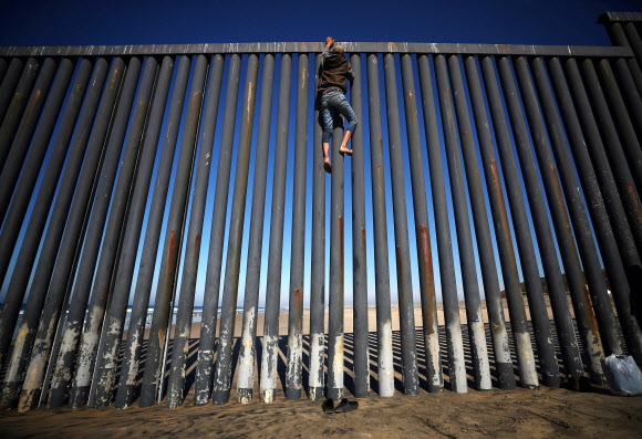 중미 출신 이민자 행렬(캐러밴)중 한 명이 18일(현지시간) 멕시코 티후아나의 미국과 멕시코 국경 펜스에 올라가고 있다. 로이터 연합뉴스