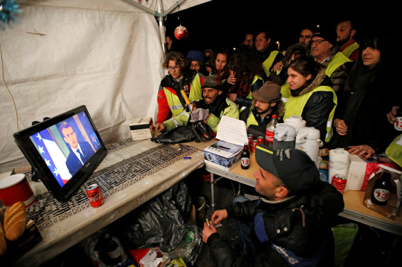 프랑스의 ‘노란 조끼’ 시위 참가자들이 10일(현지시간) 마르세유 인근의 소도시 라시오타에서 에마뉘엘 마크롱 프랑스 대통령의 대국민 담화 생방송을 시청하고 있다.  라시오타 로이터 연합뉴스