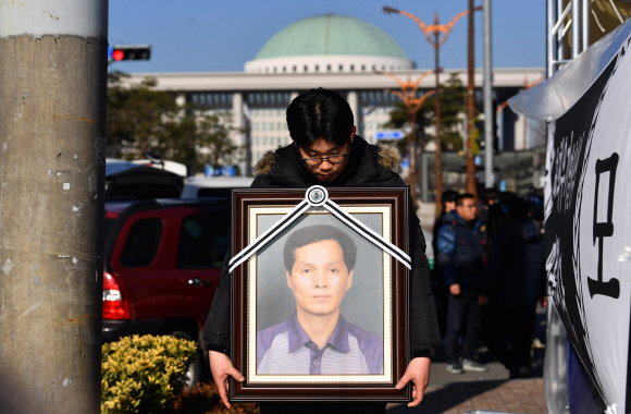 12일 서울 국회앞 국민은행에서 열린 카카오택시 카풀반대 집회에 참석한 택시업계 관계자가 분신자살한 최우기씨의 영정사진을 들고 있다. 2018.12.12 박지환기자 popocar@seoul.co.kr