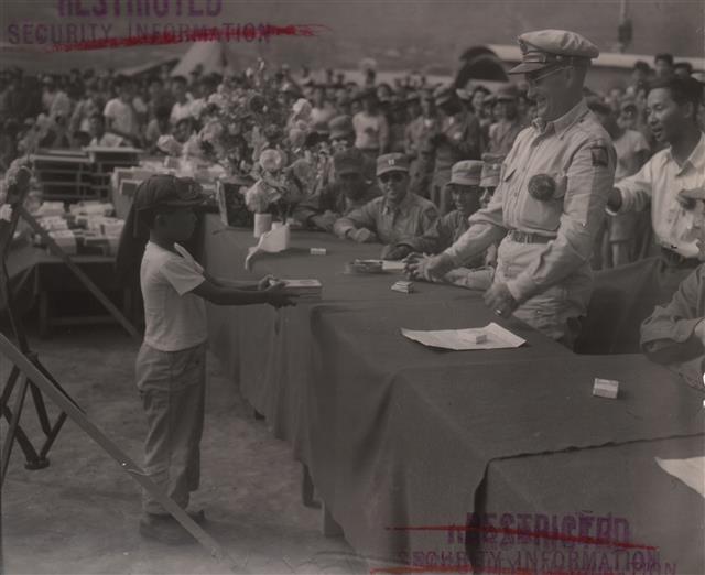 1951년 10월 경남 거제포로수용소에서 포로 대표로 나선 8살 아이가 미군 대령으로부터 재교육과 관련한 상을 받고 있다.  대한민국역사박물관 제공