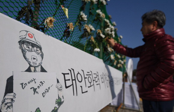 18일 충남 태안군 한국서부발전 본사 정문 옆에 마련된 김용균씨 추모 공간에서 한 시민이 고인을 추모하는 플래카드와 꽃을 바라보고 있다. 태안 박윤슬 기자 seul@seoul.co.kr