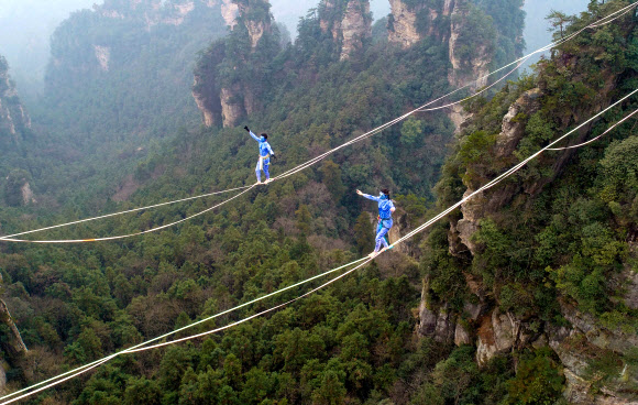 영화 ‘아바타’의 캐릭터로 분장한 두 명의 참가자가 23일(현지시간) 중국 후난 지방의 장가계에서 황시즈하이 산맥의 한가운데를 따라 레이싱하는 경기에서 줄 위를 걸어 건너고 있다. AFP 연합뉴스