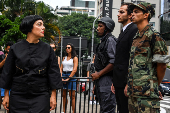 제6회 상파울루 국제연극제에 참여한 베네수엘라 태생의 예술가 데보라 카스티요(왼쪽)가 17일(현지시간) 브라질 상파울루 파울리스타 거리에서 ‘라메수엘라’라는 제목의 행위예술을 선보이는 도중 경찰과 정치인, 군인으로 분한 세 명의 남성을 바라보고 있다. 카스티요는 자신의 고국인 베네수엘라와 라메 수엘라(부츠를 핥는 사람)라는 문구를 접목한 이번 행위예술에서 니콜라스 마두로 정권의 전체주의와 억압을 폭로하고자 했다. 상파울루 AFP 연합뉴스