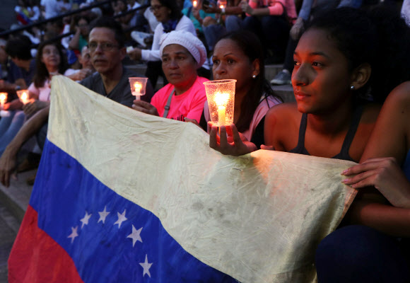 카라카스의 시민들이 5일 시내에서 열린 니콜라스 마두로 베네수엘라 대통령에게 반대하는 시위 도중 경찰의 강경진압으로 숨진 희생자들을 추모하는 촛불집회에 참석해 침통한 표정으로 국기를 들고 앉아 있다.  카라카스(베네수엘라) 로이터 연합뉴스