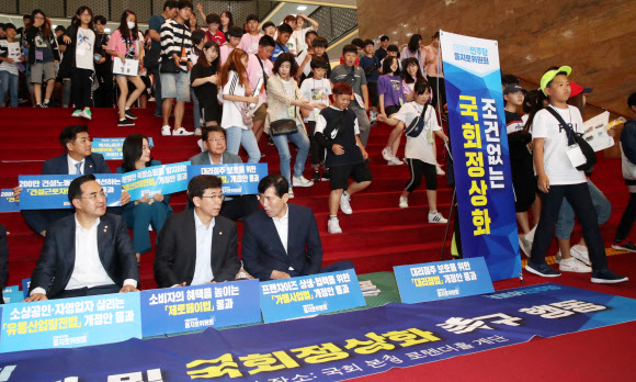 17일 국회 견학 온 어린이들이 본청 로텐더홀 계단에서 민생입법 통과 및 국회정상화 촉구하는 더불어민주당 을지로위원회 위원들 옆을 지나가고 있다. 2019.6.17 연합뉴스