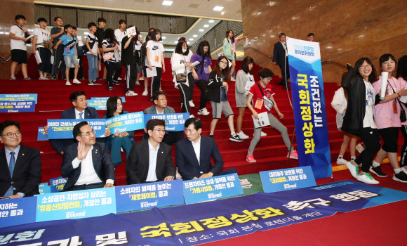 17일 국회 견학 온 어린이들이 본청 로텐더홀 계단에서 민생입법 통과 및 국회정상화 촉구하는 더불어민주당 을지로위원회 위원들 옆을 지나가고 있다. 2019.6.17 연합뉴스