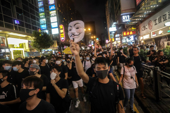 ‘범죄인인도법안’에 반대하는 홍콩의 반정부 시위대가 7일 검은 옷과 마스크를 착용한 채 쇼핑가인 몽콕의 도로를 행진하는 가운데 선두의 한 남성이 저항의 상징인 ‘가이포크스’의 마스크를 치켜들고 있다. 홍콩 AFP 연합뉴스