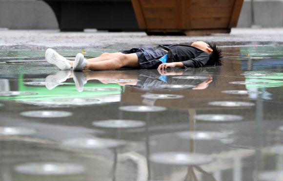 장마가 끝나고 본격적인 찜통더위가 시작된 29일 서울 종로구 광화문광장 분수대에서 물놀이를 하던  한 어린이가 누워 있다. 기상청은 이날 전국의 낮 기온이 29∼34도의 분포로 평년(28∼32도)보다 높겠다고 밝혔다. 2019.7.29  연합뉴스