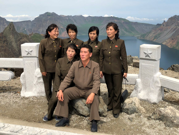 지난 24일 백두산을 방문한 북한 관광객들이 천지를 배경으로 기념사진을 찍기 위해 포즈를 취하고 있다. TASS=연합뉴스