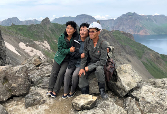 지난 24일 백두산을 방문한 북한 관광객들이 천지를 배경으로 기념사진을 찍기 위해 포즈를 취하고 있다. TASS=연합뉴스 