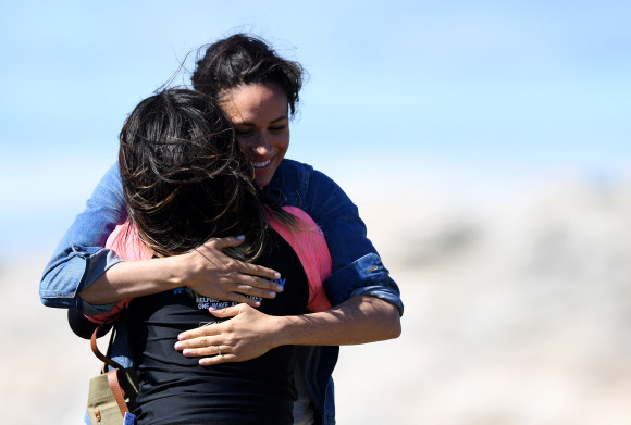 영국 메간 마클(가운데) 왕자비가 24일(현지시간) 남아프리카 케이프타운의 몬와비시 해변에서 NGO ‘Waves for Change’을 방문하는 동안 그룹 활동으로 서핑 강사 멘토들과 함께하며 포옹을 하고 있다. EPA 연합뉴스