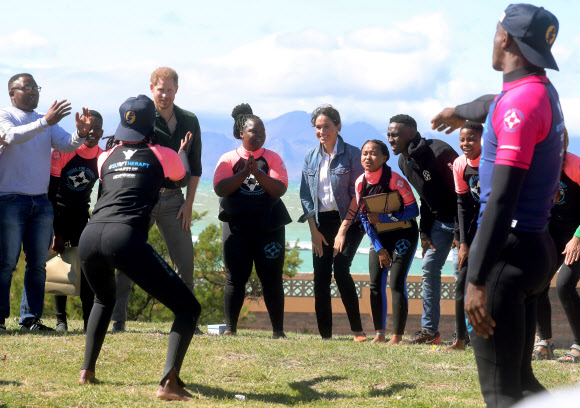 영국 해리(왼쪽 세 번째) 왕자와 메간 마클(다섯 번째) 왕자비가 24일(현지시간) 남아프리카 케이프타운의 몬와비시 해변에서 NGO ‘Waves for Change’을 방문하는 동안 그룹 활동으로 서핑 강사 멘토들과 함께하고 있다. EPA 연합뉴스