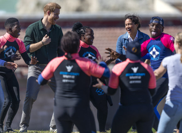 영국 해리(왼쪽 두 번째) 왕자와 메간 마클(네 번째) 왕자비가 24일(현지시간) 남아프리카 케이프타운의 몬와비시 해변에서 NGO ‘Waves for Change’을 방문하는 동안 그룹 활동으로 서핑 강사 멘토들과 함께하고 있다. EPA 연합뉴스